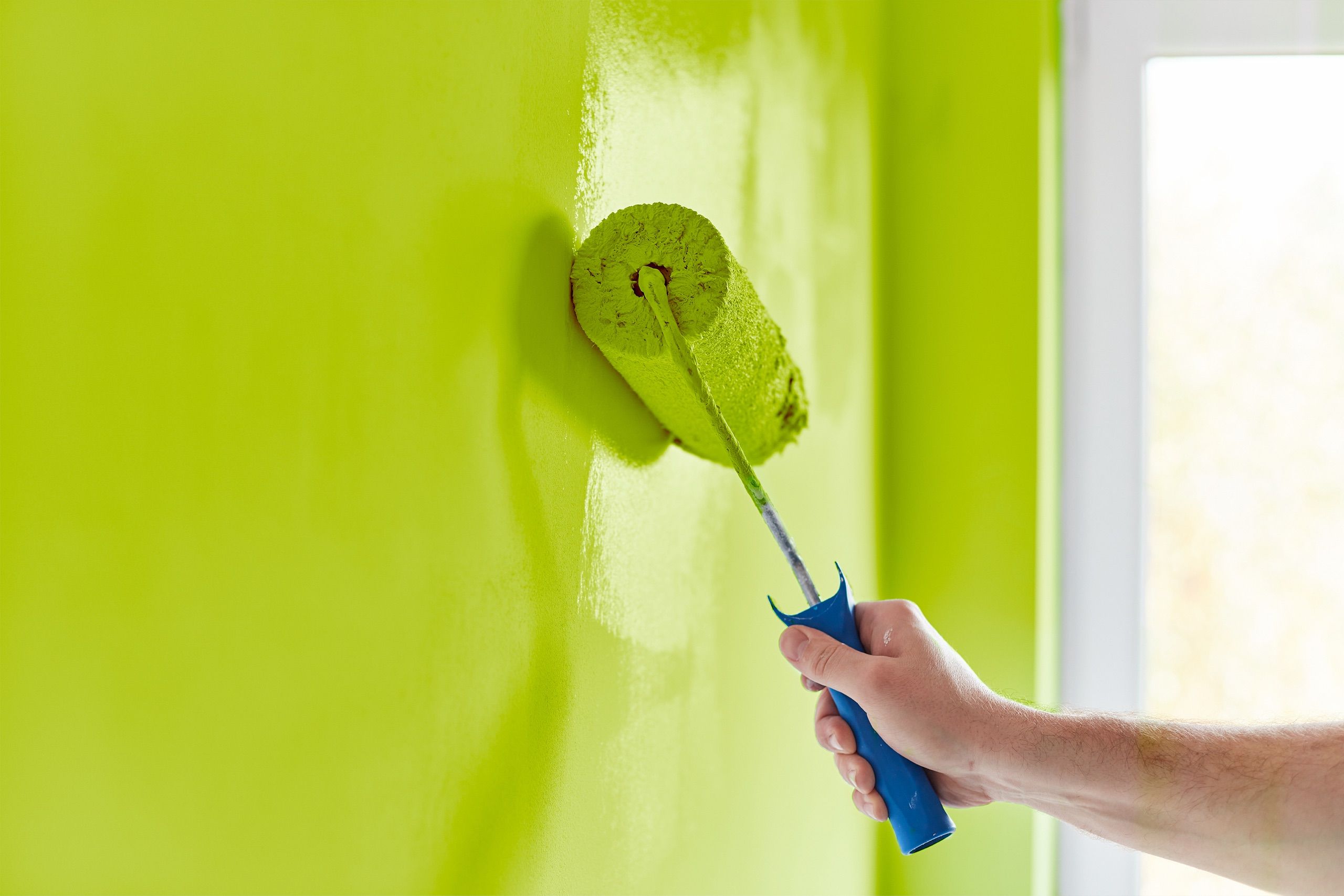Farbrolle trägt frische grüne Wandfarbe auf eine Innenwand auf